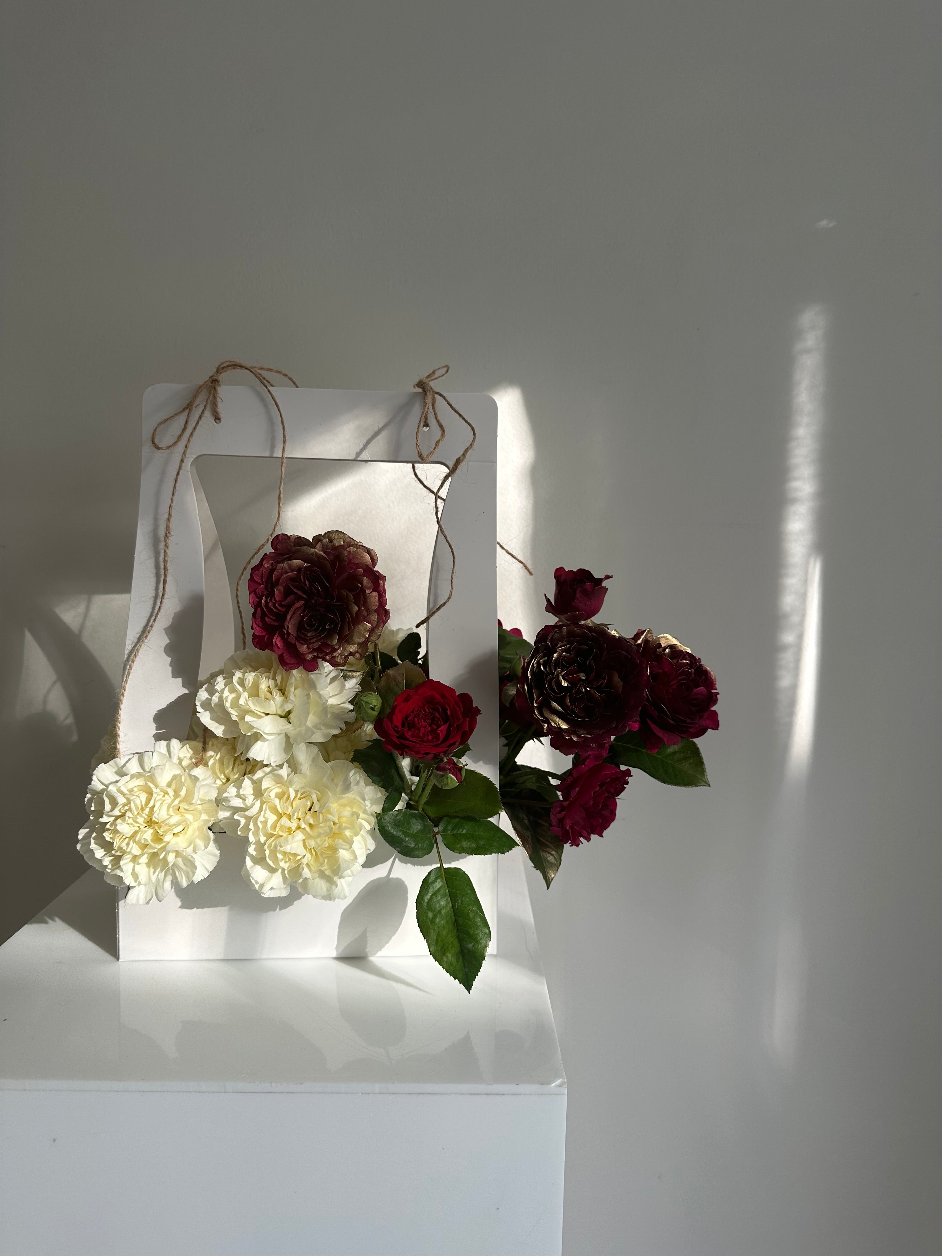 Editorial Valentine’s Day floral arrangement featuring deep red and ivory blooms styled in a sculptural white frame, photographed in natural light with soft shadows, modern romantic still life by Orkid florist.
